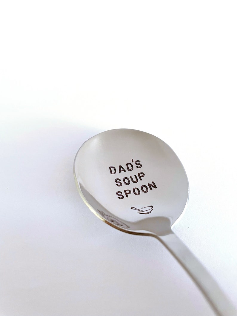 K&ouml;nnte beinhalten: Ein silberner Suppenl&ouml;ffel mit der Gravur "Dad's Soup Spoon". Unter dem Text ist ein kleines Schalen-Symbol graviert.