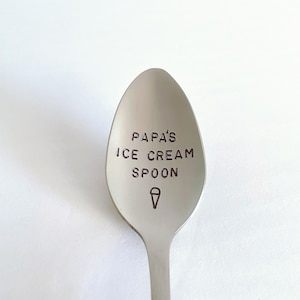 K&ouml;nnte beinhalten: Ein silberner Eis-L&ouml;ffel mit dem Text "Papa's Ice Cream Spoon" auf dem L&ouml;ffelkopf graviert. Ein Eiswaffel-Symbol ist ebenfalls auf dem L&ouml;ffelkopf graviert.