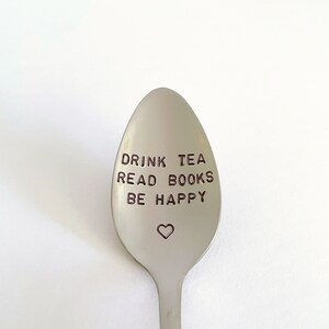 K&ouml;nnte beinhalten: Ein silberner L&ouml;ffel mit den Worten "Drink Tea Read Books Be Happy" auf der Vorderseite graviert. Ein kleines Herz ist unter dem Text graviert.