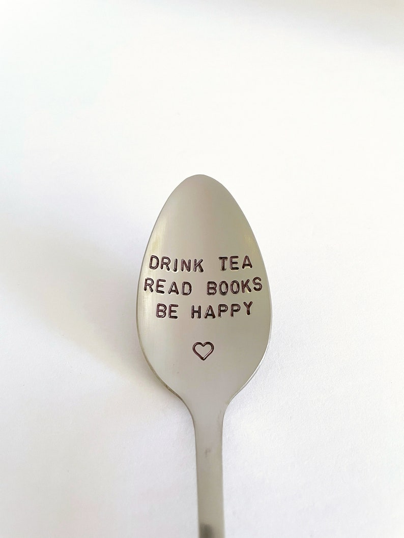 K&ouml;nnte beinhalten: Ein silberner L&ouml;ffel mit den Worten "Drink Tea Read Books Be Happy" auf der Vorderseite graviert. Ein kleines Herz ist unter dem Text graviert.