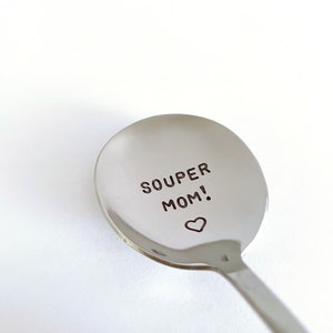 May include: A silver spoon with the words "SOUPER MOM!" engraved on the bowl, with a small heart symbol below the text.