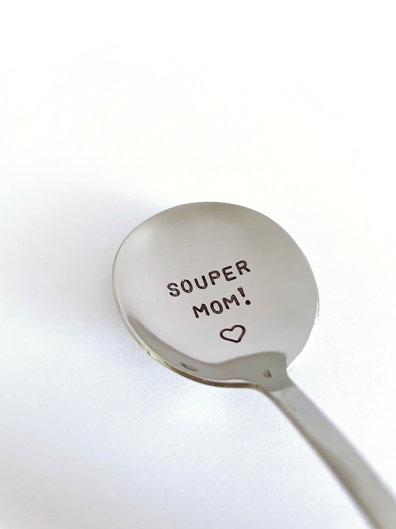 May include: A silver spoon with the words "SOUPER MOM!" engraved on the bowl, with a small heart symbol below the text.