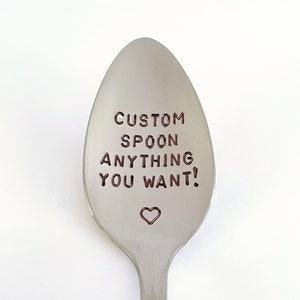 May include: A silver spoon with the text "CUSTOM SPOON ANYTHING YOU WANT!" engraved on the front. A small heart is engraved below the text.