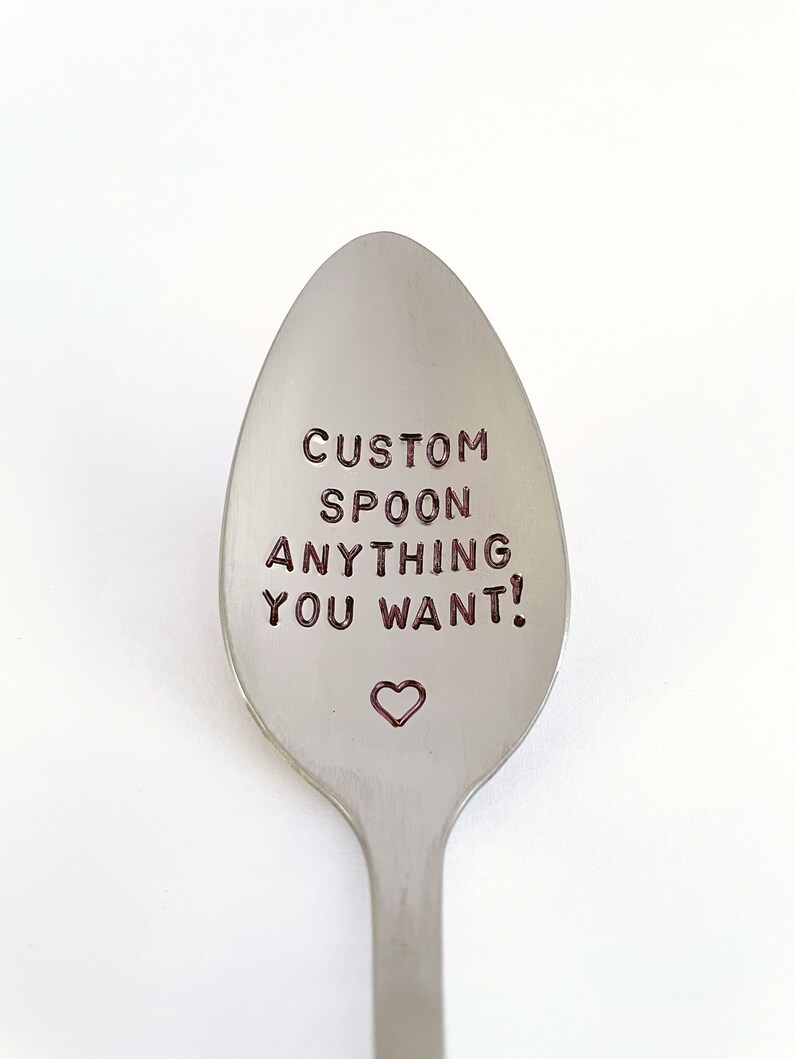 May include: A silver spoon with the text "CUSTOM SPOON ANYTHING YOU WANT!" engraved on the front. A small heart is engraved below the text.