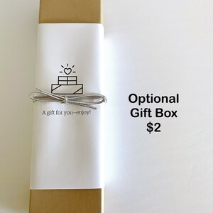 May include: A gold gift box with a white label that says "A gift for you - enjoy!" and has a simple line drawing of a gift box with a heart on top. The text "Optional Gift Box $2" is printed below the box.