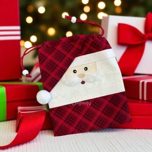 Könnte beinhalten: Ein rot-schwarz karierter Geschenkbeutel mit Kordelzug und einem Weihnachtsmann-Gesicht. Das Gesicht des Weihnachtsmanns ist weiß mit gestickten Details und einem flauschigen weißen Bart. Der Beutel hat einen roten Kordelzugverschluss und einen weißen Bommel.