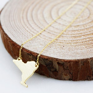 May include: A gold necklace with a pendant shaped like the state of New York. The necklace is on a wooden surface.