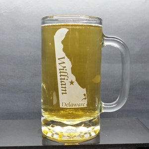 May include: A clear glass beer mug with a handle. The mug is etched with the outline of the state of Delaware, a star, and the text "William Delaware".