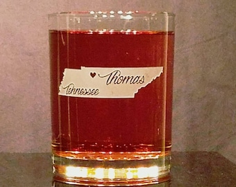May include: A clear glass tumbler filled with a reddish-brown liquid. The glass features a white label with a map outline of Tennessee, the word "Tennessee", a heart symbol, and the name "Thomas".