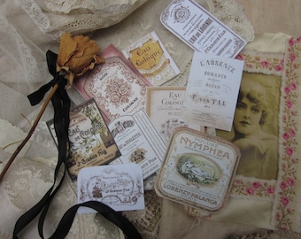 May include: Vintage style perfume and cologne labels with floral designs and text in French. The labels are printed on cream-colored paper and have a distressed look. The labels are arranged on a piece of fabric with a lace overlay.