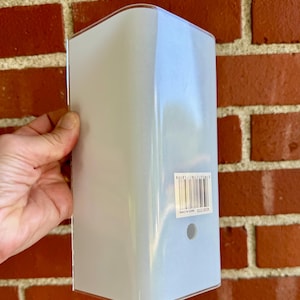 May include: A rectangular, light blue plastic wall-mounted light fixture cover with rounded vertical edges. The surface features a white barcode sticker with the number 40361213 and a small circular hole positioned near the bottom center.