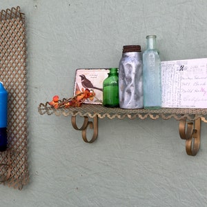 May include: A vintage-style wall shelf and candle holder set. The shelf is made of gold-toned metal with a decorative edge, holding bottles, a postcard, and a small picture. A blue candle sits in a matching holder.