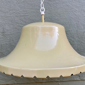 May include: Cream-colored, vintage pendant light fixture. The light has a bell-shaped shade with a flared bottom and decorative cutouts. It hangs from a white chain and a matching ceiling mount. The fixture is made of metal and has a glossy finish.