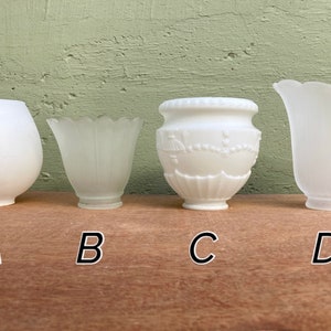 May include: Four white glass lamp shades labeled A, B, C, and D. Shade A is a smooth globe. Shade B is a fluted, frosted bell. Shade C is an opaque white urn with embossed floral garlands and vertical ribs. Shade D is a wide, frosted, scalloped bell.