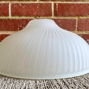 May include: A dome-shaped lamp shade made of frosted white glass featuring a series of vertical, raised ribbing patterns that extend from the center opening down to the smooth, circular bottom edge of the fixture.
