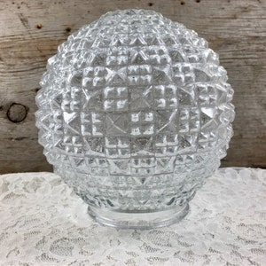 May include: Clear glass globe light fixture with a geometric diamond pattern. The round shade has a wide base and a textured surface. The light fixture is suitable for a ceiling light or pendant light.