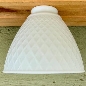 May include: A white, diamond-patterned glass lampshade. The shade has a rounded, bell-like shape and a smooth, circular base. The lampshade is made of opaque glass and is designed to diffuse light.