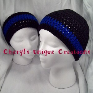 May include: Two crocheted hats with a black and blue stripe design. The hats are on white mannequins. The text "Cheryl's Unique Creations" is visible in the image.