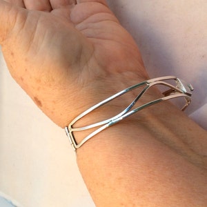 May include: A silver bangle bracelet with a geometric design. The bracelet is open and has a hinge closure.
