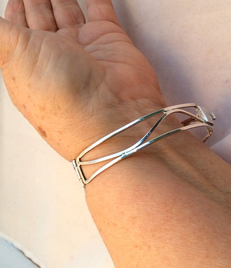May include: A silver bangle bracelet with a geometric design. The bracelet is open and has a hinge closure.