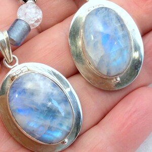 May include: Two oval-shaped moonstone pendants set in silver. The moonstones are a pale blue color with a shimmery iridescent effect.