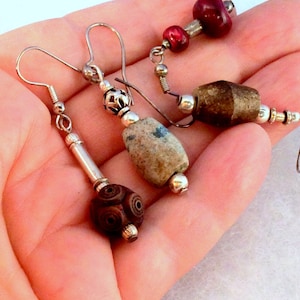 May include: Three pairs of earrings with different styles and colors. The first pair features a brown wooden bead with a swirl pattern. The second pair has a light blue and gray stone bead. The third pair has a red and brown wooden bead.