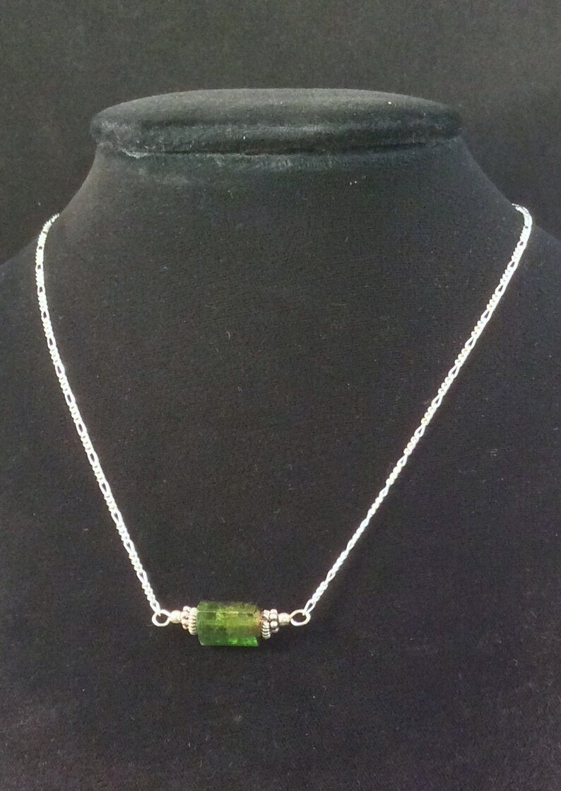 Op de afbeelding: Een zilveren ketting met een enkele groene edelsteen hanger.