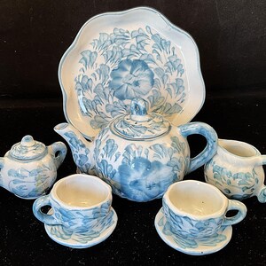 May include: A miniature ceramic tea set with a floral design in shades of blue and white. The set includes a teapot, creamer, sugar bowl, two teacups with saucers, and a serving platter.