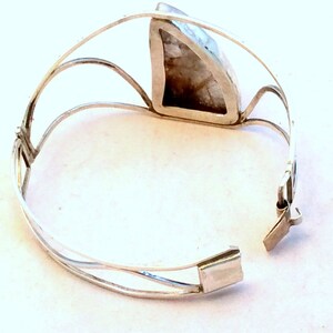 May include: Silver bracelet with a large, triangular, opaque, white gemstone set in the center. The bracelet has a hinged clasp.