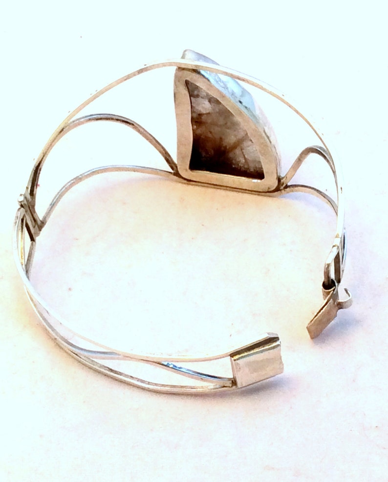 May include: Silver bracelet with a large, triangular, opaque, white gemstone set in the center. The bracelet has a hinged clasp.