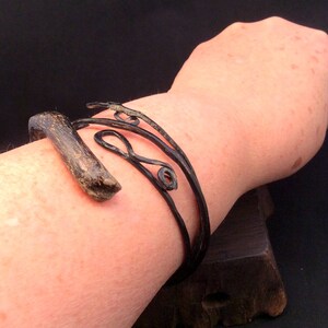 May include: A black metal bracelet with a unique, organic design. The bracelet is made of twisted wire and has a smooth, polished finish.