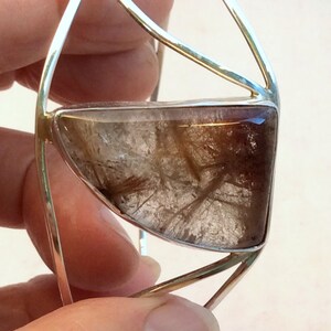 May include: A silver bangle bracelet with a clear, faceted, brown and white gemstone. The gemstone is set in a silver frame.