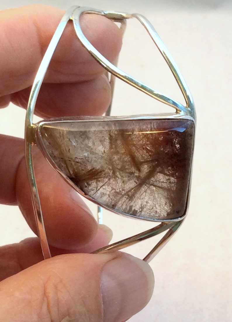 May include: A silver bangle bracelet with a clear, faceted, brown and white gemstone. The gemstone is set in a silver frame.