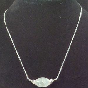 Op de afbeelding: Een zilveren ketting met een ovale hanger van helder kwarts.
