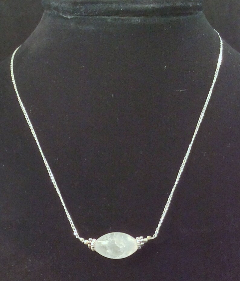 Op de afbeelding: Een zilveren ketting met een ovale hanger van helder kwarts.