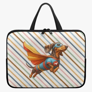 Op de afbeelding: Zwarte laptoptas met een kleurrijk strepenpatroon. De tas heeft een cartoonillustratie van een teckel verkleed als superheld, compleet met cape en masker. De hond wordt vliegend afgebeeld.