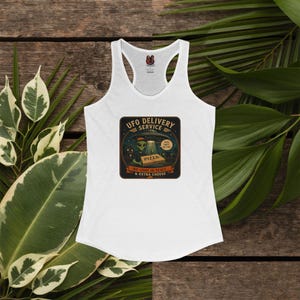 Puede incluir: Una camiseta de tirantes blanca con espalda nadadora y un estampado gráfico de un alienígena sosteniendo una caja de pizza bajo un OVNI. El texto dice UFO DELIVERY SERVICE, FAST QUIET NO TIPS y WE COME IN PEACE & EXTRA CHEESE en verde, naranja y negro.