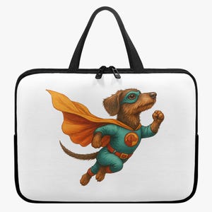 Op de afbeelding: Een witte laptoptas met zwarte rand en handvatten. De tas heeft een cartoonillustratie van een teckel verkleed als superheld, met een turquoise en oranje kostuum en een blauw masker.