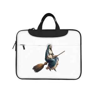 Può includere: Una custodia bianca per laptop con manico e cerniera neri. La custodia presenta un'illustrazione di una donna in abiti blu che cavalca una scopa. La donna ha un'aureola e tiene in mano un bastone di legno.