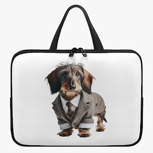 Op de afbeelding: Witte laptoptas met zwarte rits en handvatten. De tas heeft een grillige illustratie van een teckel in een tweed pak, stropdas en overhemd. De hond staat op een witte achtergrond.