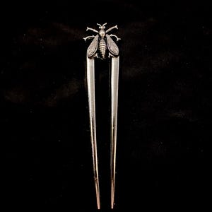 May include: Silver hair pin with a bee motif. The pin has two long, parallel prongs, and the bee is at the top. The bee design has detailed wings and body, adding a touch of nature-inspired elegance to the hair accessory.