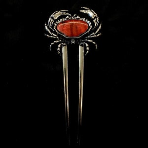 May include: Silver hair comb with a crab design and a red gemstone in the center.