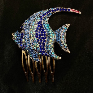 May include: A blue and iridescent jeweled fish hair comb with a gold-tone finish. The comb has five teeth.