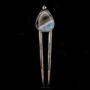 May include: A silver hair stick with a teardrop-shaped blue and black agate stone at the top.