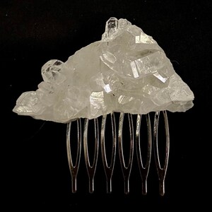 May include: A clear quartz crystal comb with a silver metal comb base. The crystal is a cluster of points and is a natural, raw, and unpolished stone.
