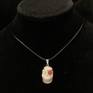 May include: A white skull pendant necklace with a red rhinestone eye patch. The necklace has a black cord.