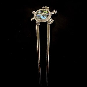 May include: Silver hair stick with a decorative turtle head at the top. The turtle's shell is made of iridescent abalone and has a border of clear rhinestones.