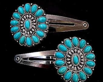 May include: Two silver-toned hair clips, each featuring a circular decorative element adorned with a central oval turquoise-colored stone surrounded by a ring of smaller, petal-shaped turquoise-colored stones set in a scalloped metal frame.
