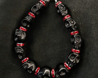 May include: Black skull bead bracelet with red rhinestone accents. The bracelet is made of black beads that are shaped like skulls. Each skull bead has a band of red rhinestones around it.