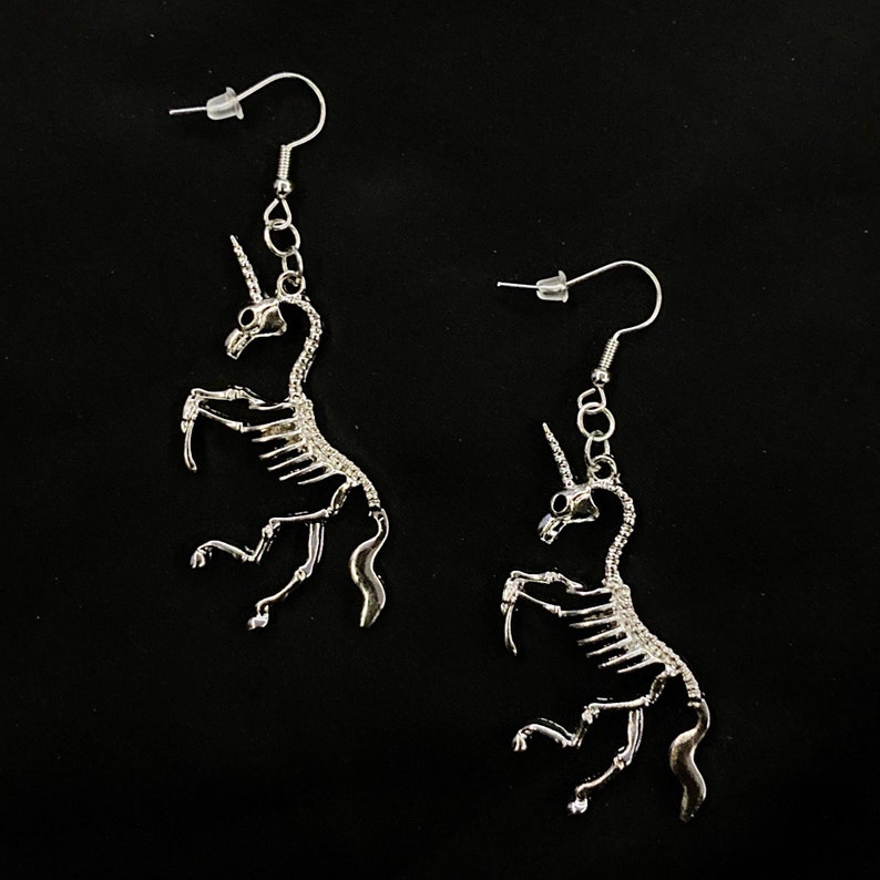 May include: A pair of silver skeleton unicorn earrings. The earrings are dangling and feature a detailed skeleton design of a unicorn.